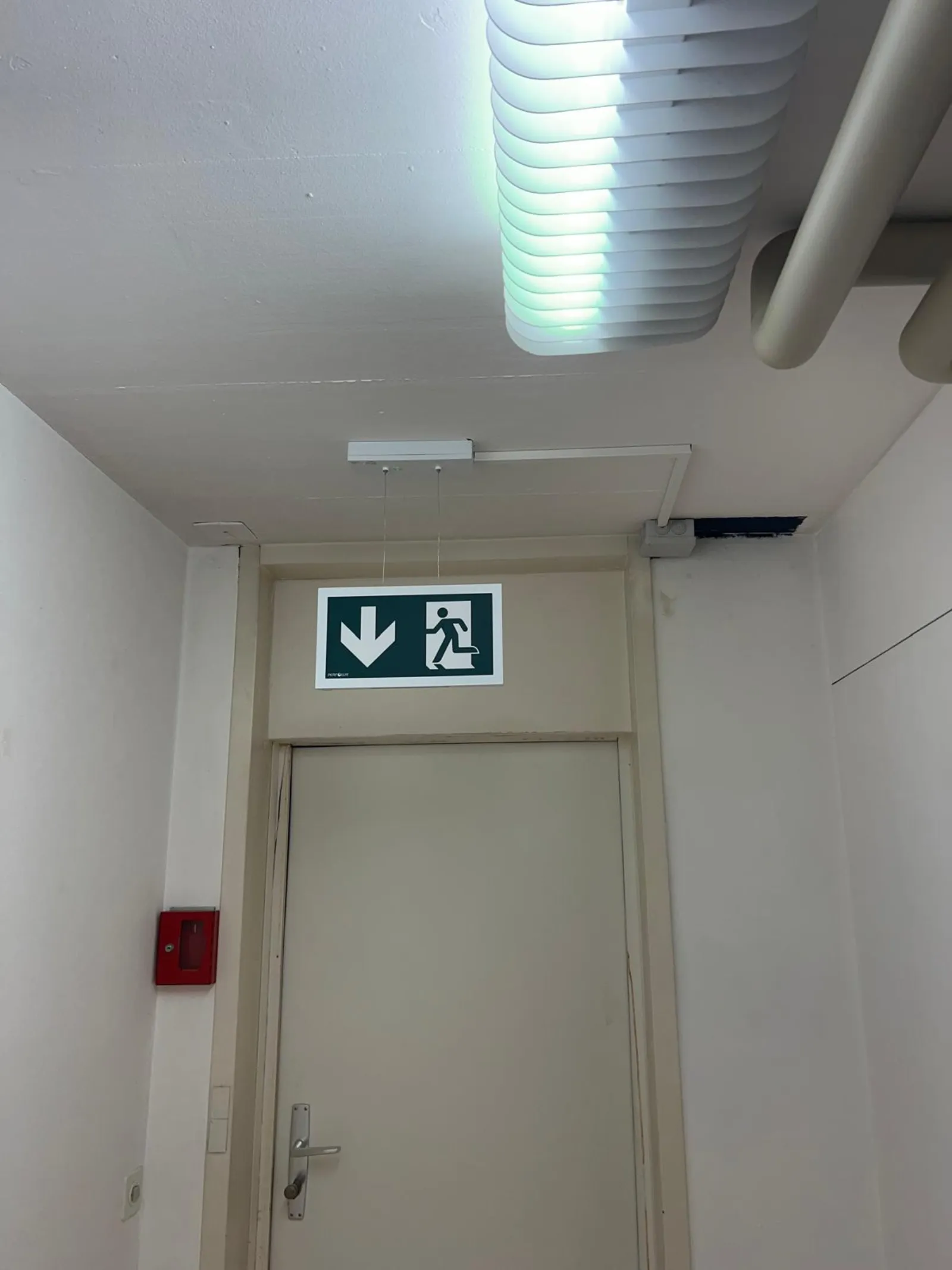Pictogramme et BAES installés au-dessus d'une porte de sortie de secours