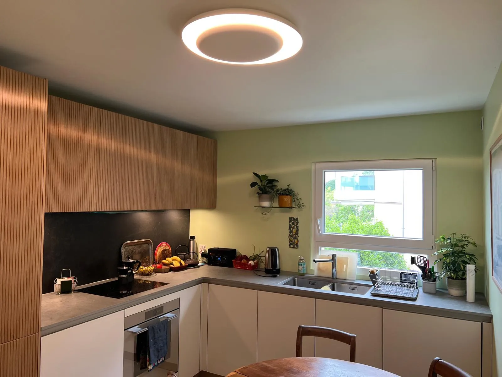 Cuisine moderne bois clair canneluré, mur vert sauge, plafonnier rond LED — après rénovation