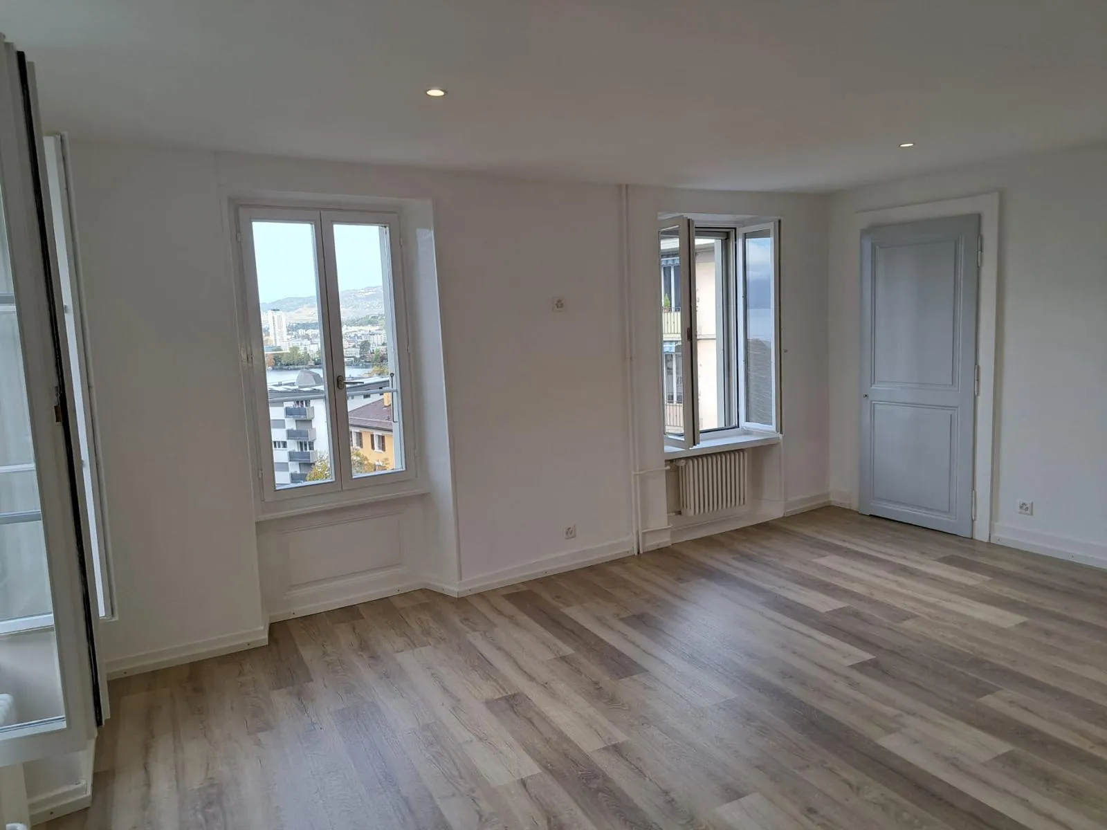 Salon rénové avec sol bois clair et fenêtres anciennes après rénovation